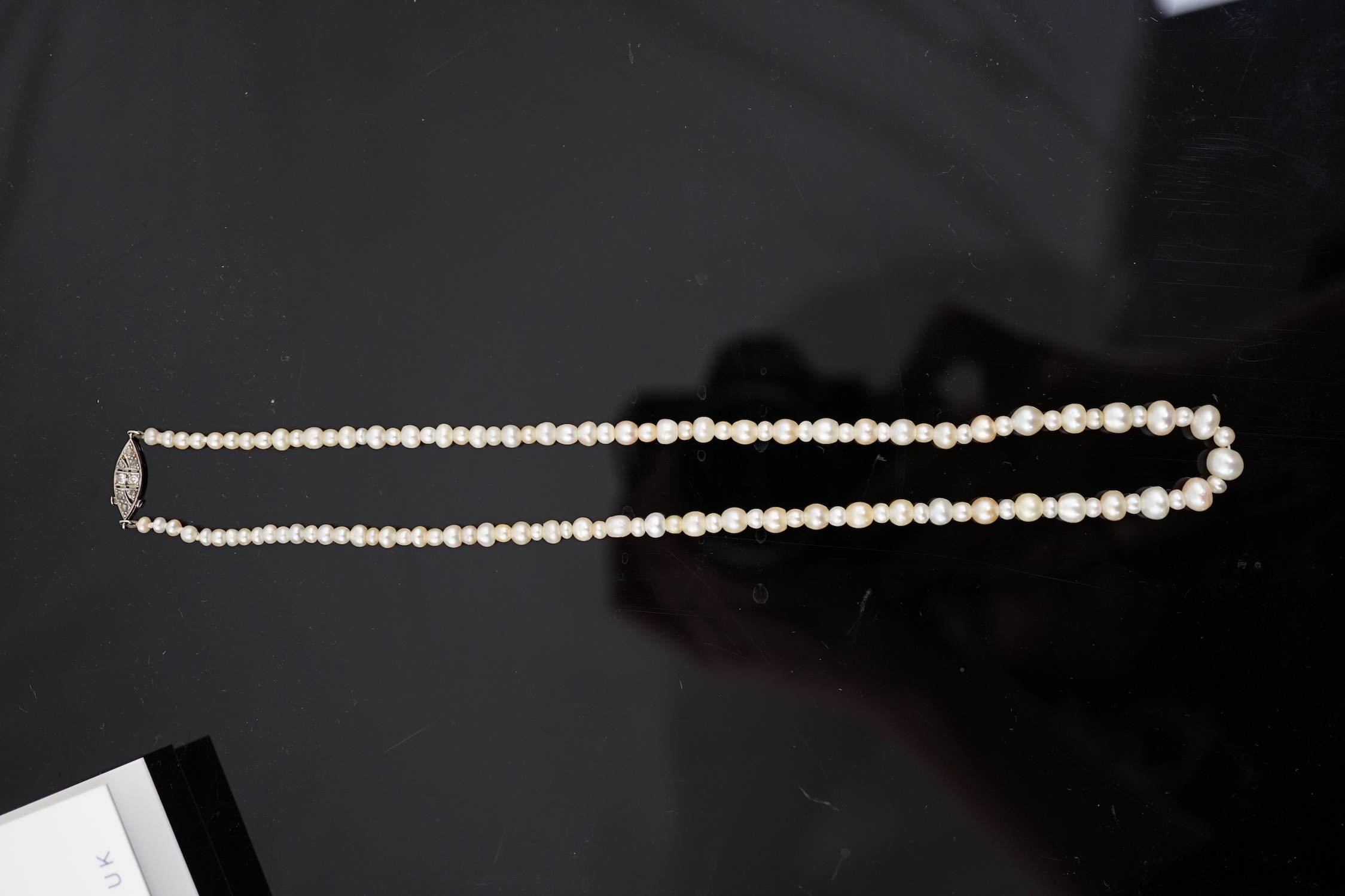 A late 19th century single strand graduated natural saltwater pearl necklace, with a French 18ct white gold and millegrain set diamond marquise shaped clasp